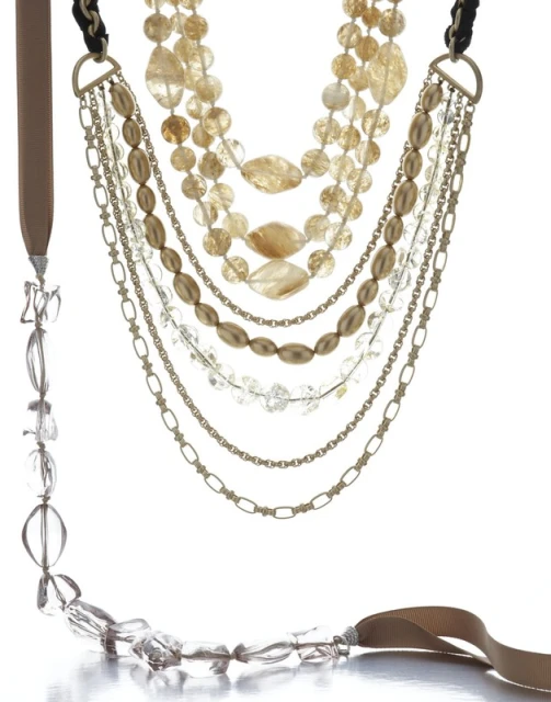 Multi-strand statement necklace featuring gold chains, various tan, gold, and clear beads, and a tan ribbon on a white background.
