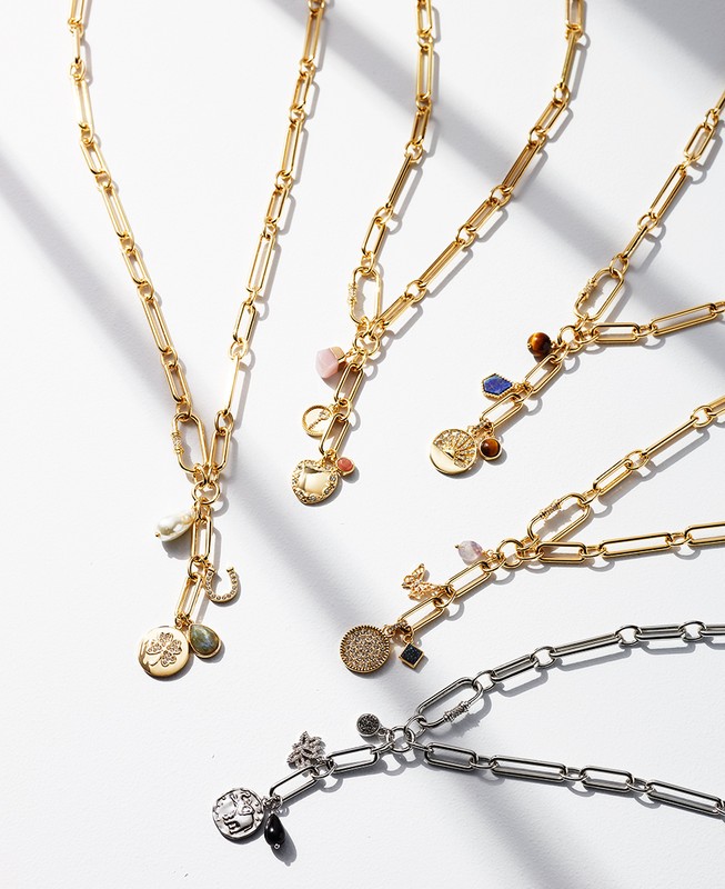 Close-up studio shot of a collection of gold and silver pendant necklaces with charms on a white surface with shadows. Fashion shot.