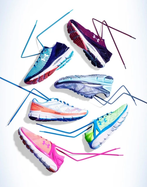 Several colorful Under Armour running shoes and laces are arranged against a bright white backdrop in a product shot.