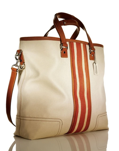 Ivory tote bag with brown leather handles and vertical stripes. Fashionable purse on reflective surface against white backdrop.