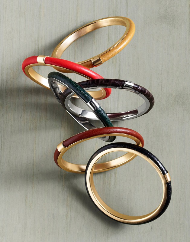 Stack of six colourful metal and leather bangles arranged diagonally on a textured wooden background styled by Kate Mccann