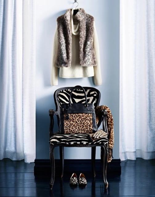 Fashion still life featuring an animal print purse and shoes on a zebra patterned chair in front of white curtains and blue wall.
