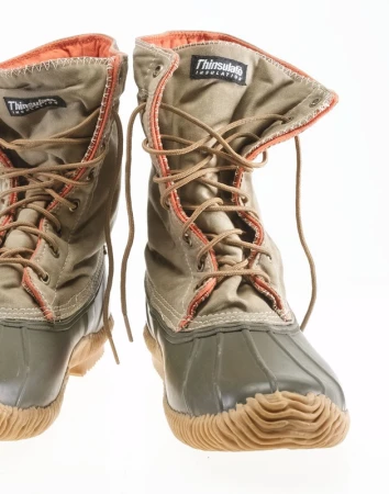 Pair of tan and olive green duck boots with brown laces on a white backdrop, showcasing outdoor footwear with durable construction.