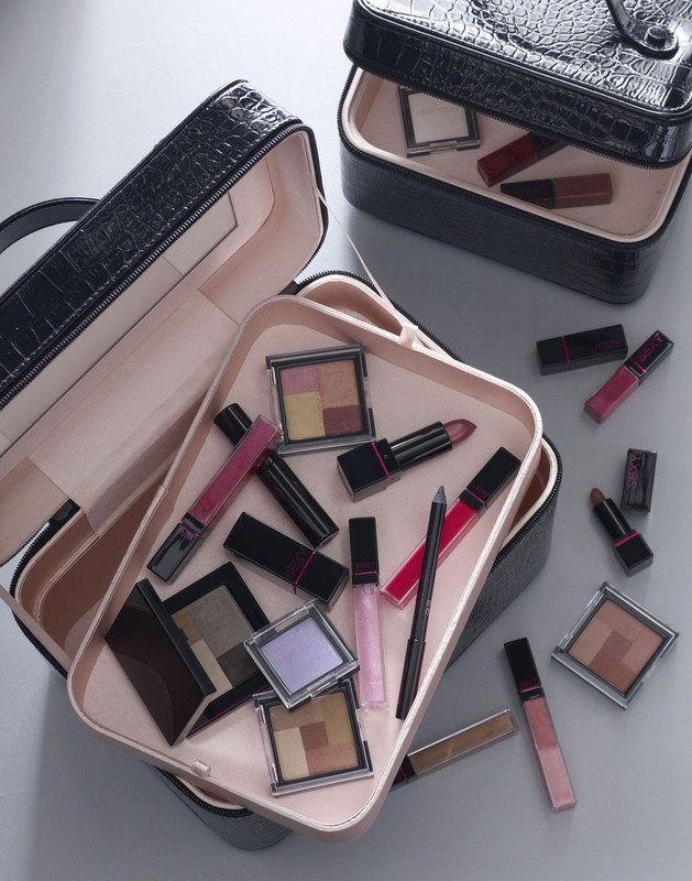 Overhead shot of open black makeup organizer cases filled with cosmetic products on a gray surface, enhancing beauty aesthetic.