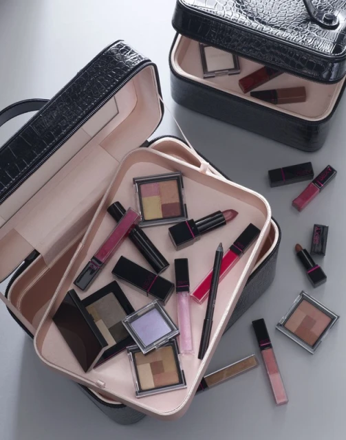 Overhead shot of open black makeup organizer cases filled with cosmetic products on a gray surface, enhancing beauty aesthetic.