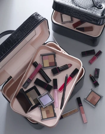 Overhead shot of open black makeup organizer cases filled with cosmetic products on a gray surface, enhancing beauty aesthetic.