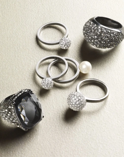 Collection of silver rings with crystal and pearl accents on a light surface, showcasing elegant and modern jewelry design.