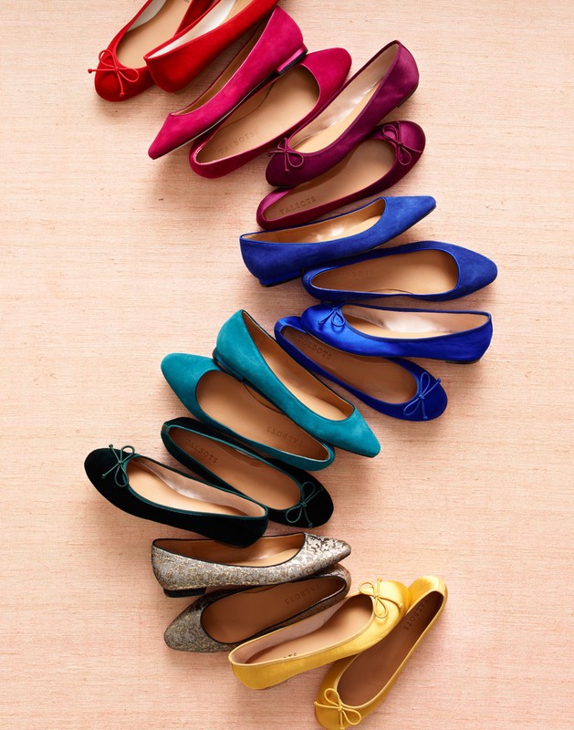 Collection of colorful ballet flats arranged diagonally on a light pink surface, showcasing a variety of hues and textures.