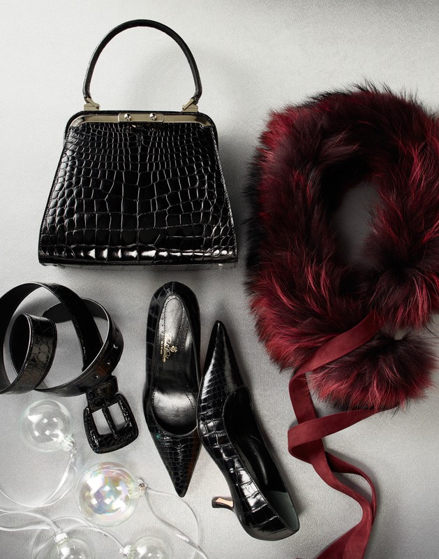 Fashion still life featuring a black crocodile leather handbag, black pumps, a belt, a faux fur scarf with ribbon, and decorative lights.