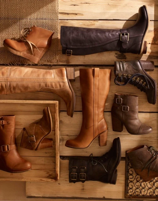 Collection of women's leather boots in various styles arranged on a wooden surface with natural light highlighting textures and details.