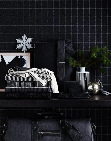 Stacked sweaters, a tie, gloves, an ornament, and a duffel bag on a shelf against a black and gray plaid wallpaper backdrop.