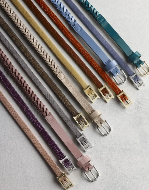 Array of colorful thin belts with various textures and braided designs, all arranged on a flat surface with silver or gold buckles.