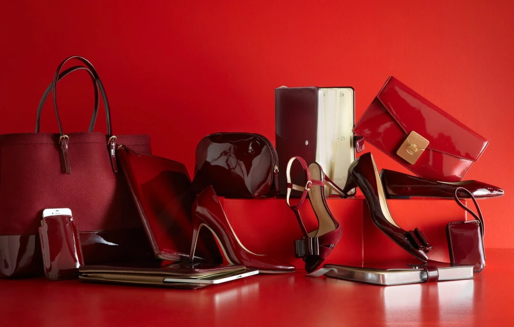 Fashionable accessories, including purses, high heels, and tech accessories, arranged on a red background for a coordinated aesthetic.