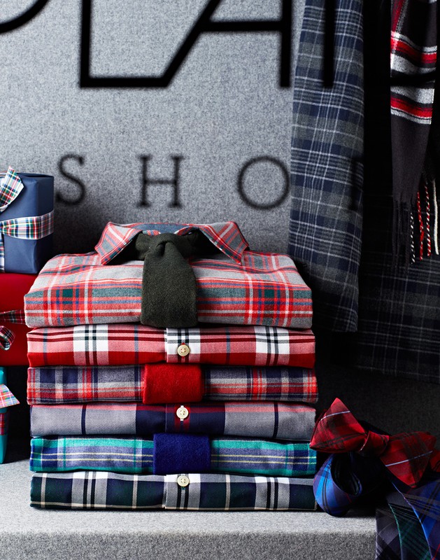 Stack of colorful plaid shirts and wrapped gifts with dark gray background, showcasing men's fashion apparel and holiday gift ideas.