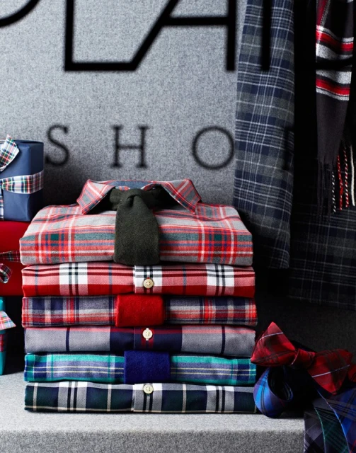 Stack of colorful plaid shirts and wrapped gifts with dark gray background, showcasing men's fashion apparel and holiday gift ideas.