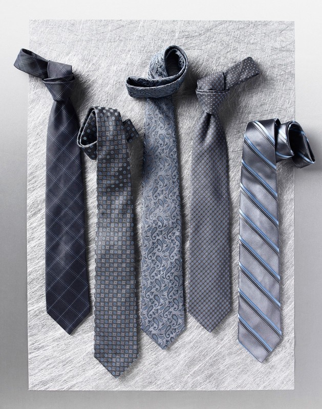 Five assorted grey neckties with different patterns arranged vertically on a textured surface.