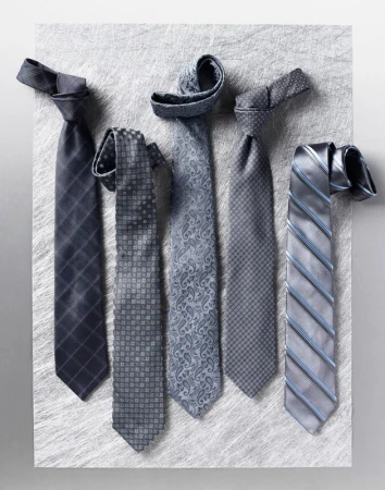 Five assorted grey neckties with different patterns arranged vertically on a textured surface.