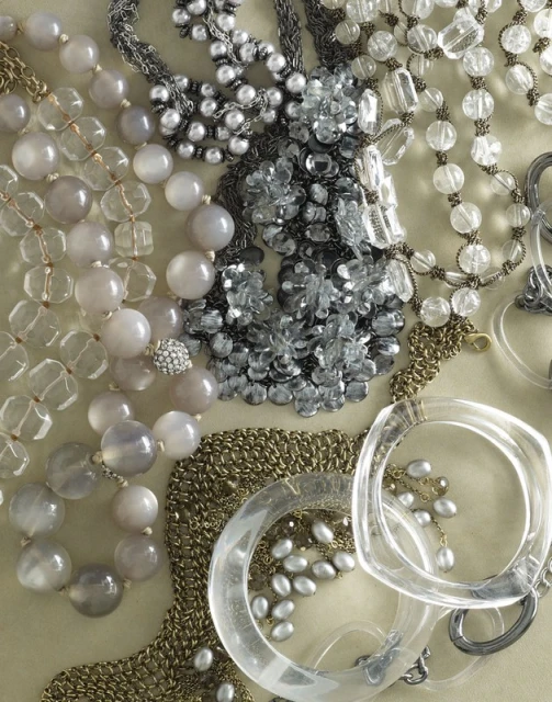 Assorted necklaces and bracelets of various materials, including beads, crystals, and clear bangles, displayed on a neutral surface.