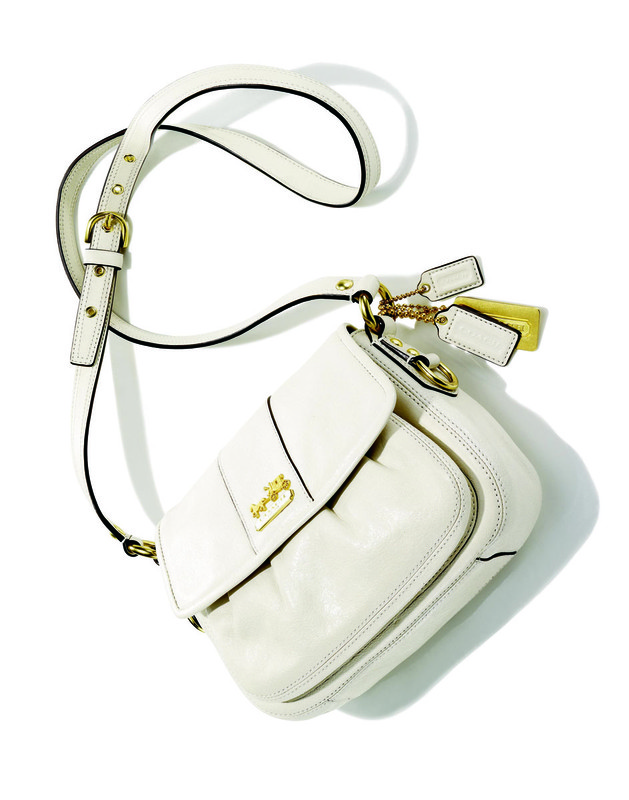 Ivory Coach brand shoulder bag with gold hardware, adjustable strap, and brand tag on a white background in a studio shot.