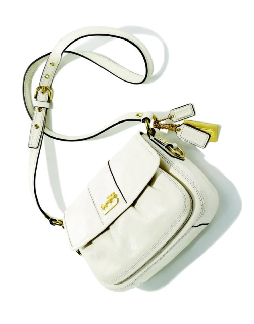 Ivory Coach brand shoulder bag with gold hardware, adjustable strap, and brand tag on a white background in a studio shot.