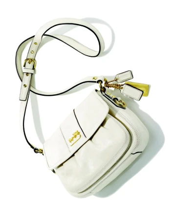 Ivory Coach brand shoulder bag with gold hardware, adjustable strap, and brand tag on a white background in a studio shot.