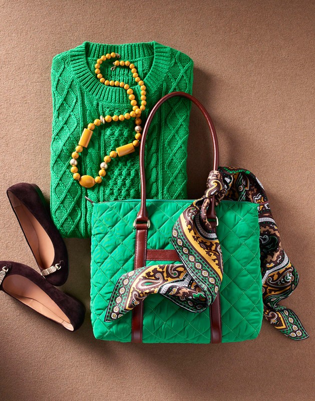 Flat lay of a green quilted handbag, matching cable knit sweater, yellow beaded necklace, patterned scarf, and brown flats.