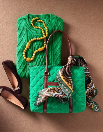 Flat lay of a green quilted handbag, matching cable knit sweater, yellow beaded necklace, patterned scarf, and brown flats.