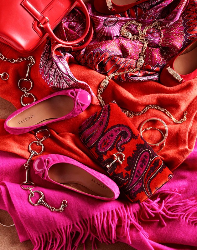 Flat lay of pink ballet shoes, a red purse, patterned scarf, and gold jewelry on colorful textile backgrounds. Fashion accessories.