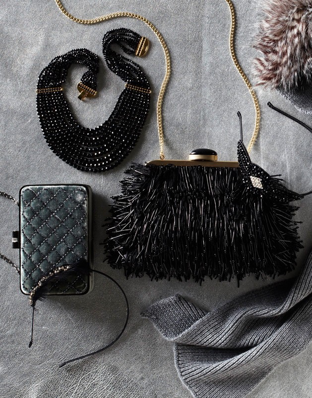 Black beaded necklace and fringe purse with chain strap are staged with a quilted wallet and gray wool scarf on a gray background.