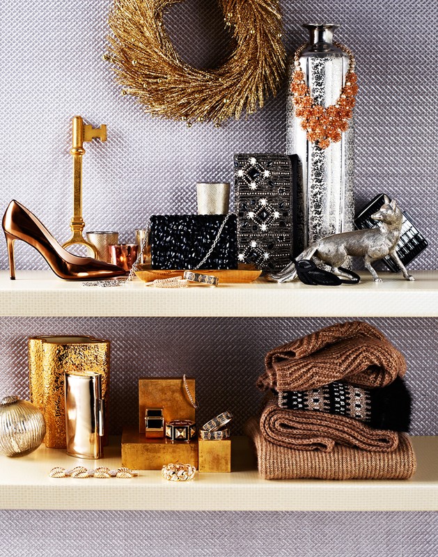 Elegant still life arrangement of gold accessories, jewelry, handbags, and shoes on shelves against a textured gray wall.