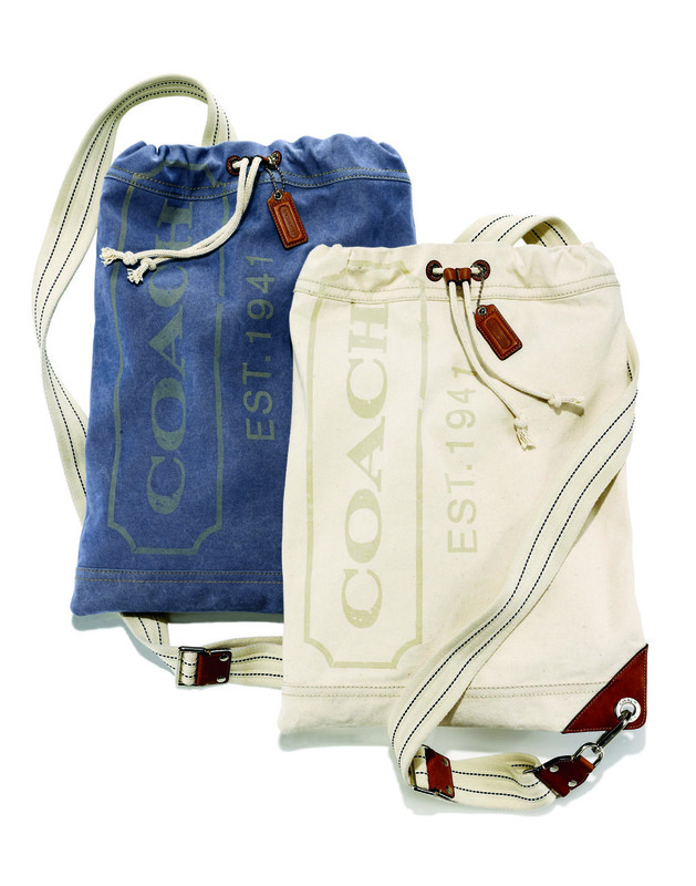 Two Coach drawstring backpacks in blue and cream canvas with leather accents and striped shoulder straps against a white backdrop.