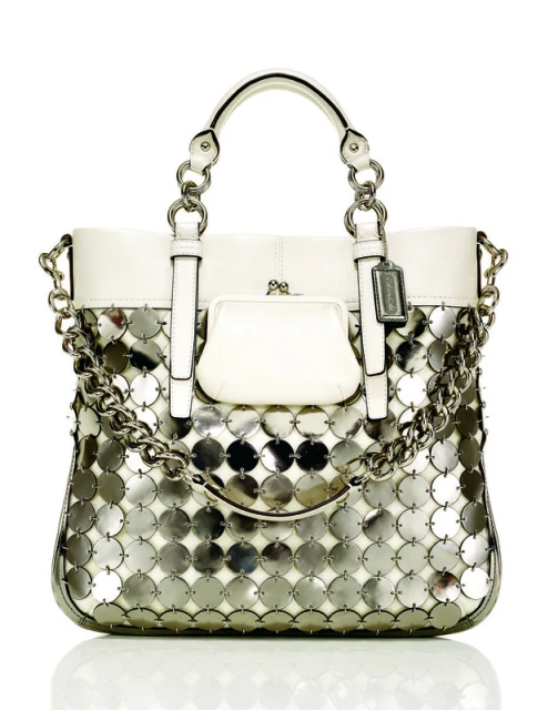 White Coach purse with silver circular sequin detail and silver chain. Fashion accessory with top handles on a white background.