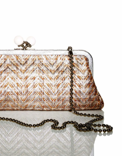 Elegant woven clutch handbag with beaded handle on a reflective white surface, studio shot, stylish fashion accessory.