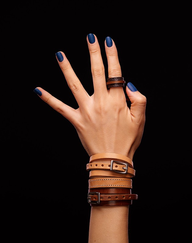 Close-up of a fair-skinned hand displaying leather accessories: a brown ring on the index finger and multiple buckled bracelets.