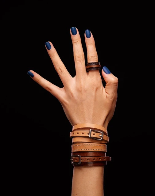 Close-up of a fair-skinned hand displaying leather accessories: a brown ring on the index finger and multiple buckled bracelets.