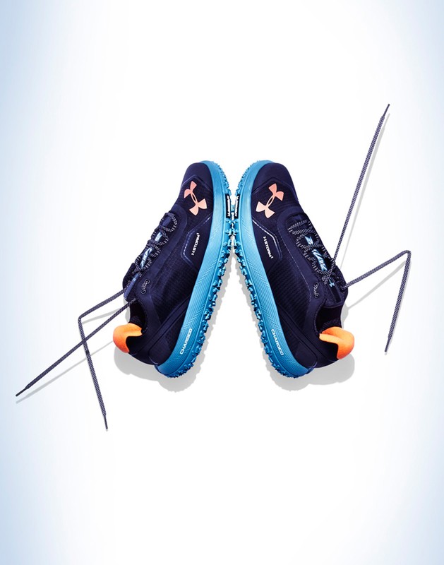 Overhead shot of a pair of dark blue Under Armour running shoes with blue midsoles and peach accents, set against a white background.