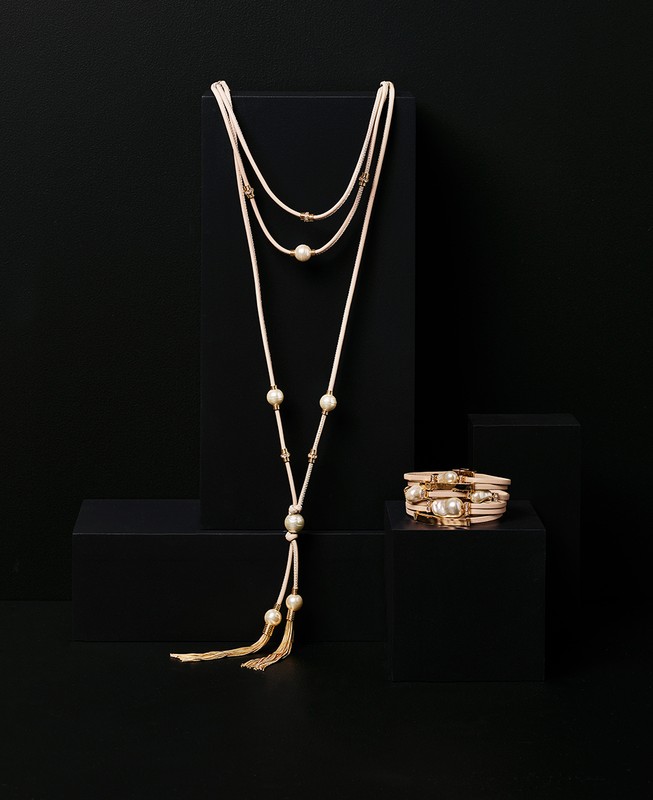 Elegant necklace and bracelet with pearl accents displayed on a black pedestal against a dark background, jewellery fashion photography.