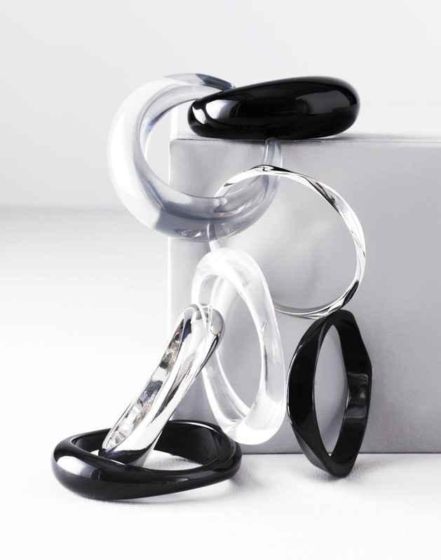 Abstract still life of clear and black bracelets arranged on a geometric white surface against a gradient background for a studio jewelry shoot.