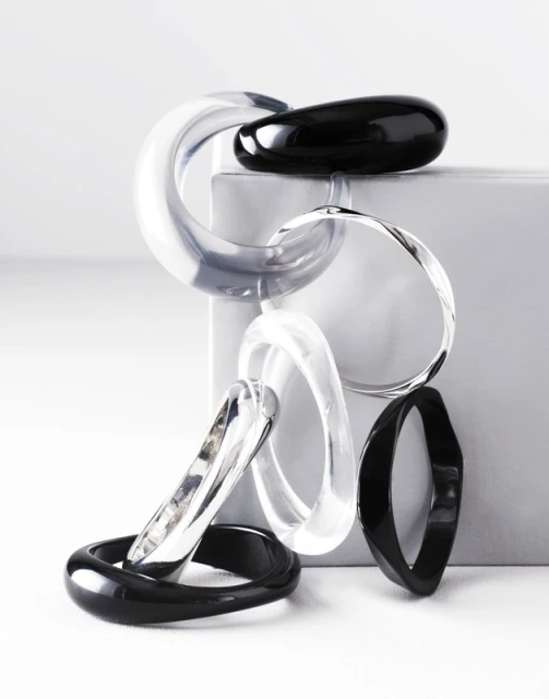 Abstract still life of clear and black bracelets arranged on a geometric white surface against a gradient background for a studio jewelry shoot.