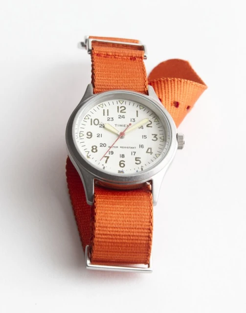 Wristwatch featuring a silver casing, white dial with black numerals, and an orange nylon strap, presented on a plain white background.