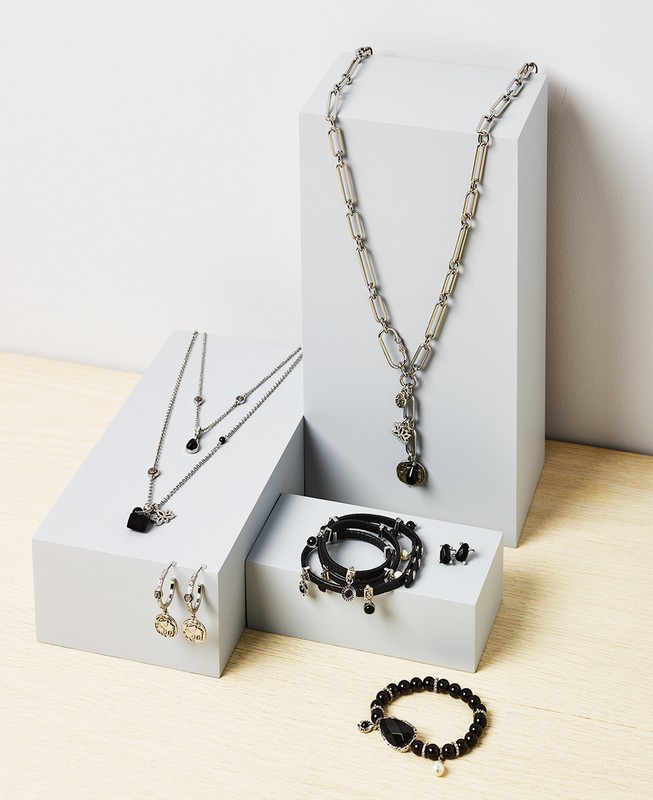 Assortment of necklaces, bracelets, and earrings displayed on white geometric risers against a two-tone background; jewelry concept.