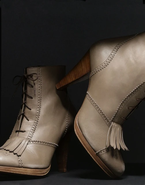 Two high-heeled ankle boots with lace-up fronts and wooden heels sit against a dark gray background in a studio product shot.