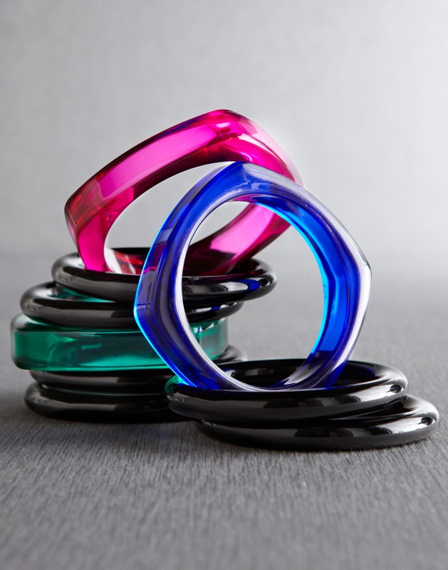 Stack of colorful square bangles in pink, blue, green, and black on a gray surface, jewelry, accessories, high-key product shot.