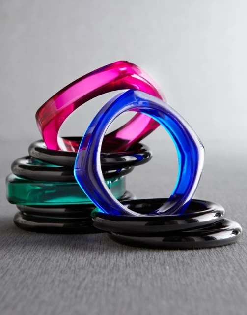 Stack of colorful square bangles in pink, blue, green, and black on a gray surface, jewelry, accessories, high-key product shot.