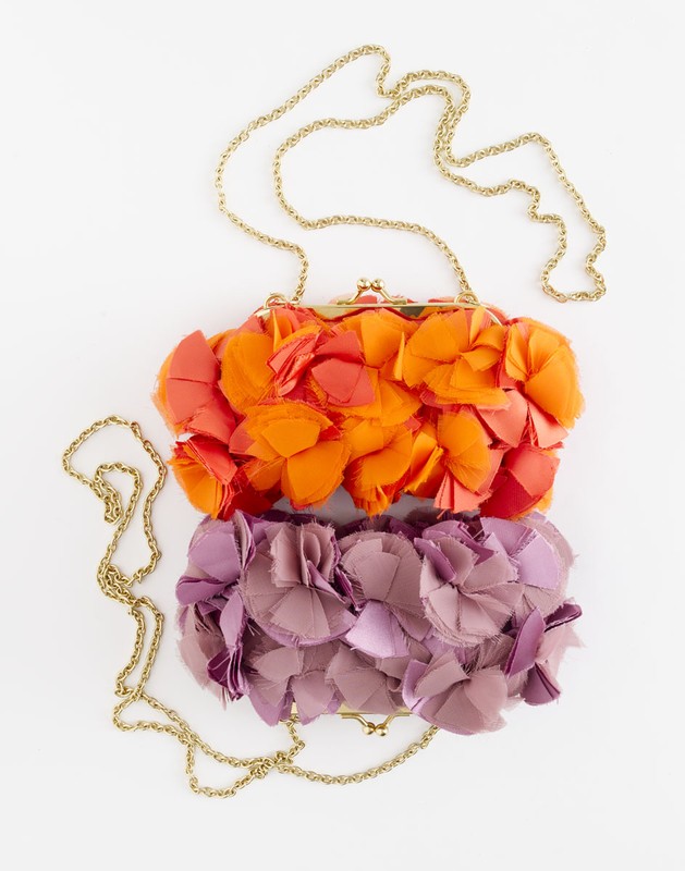 Two flower-embellished clutches with gold chain straps are stacked on a white surface, showcasing orange and purple floral designs.