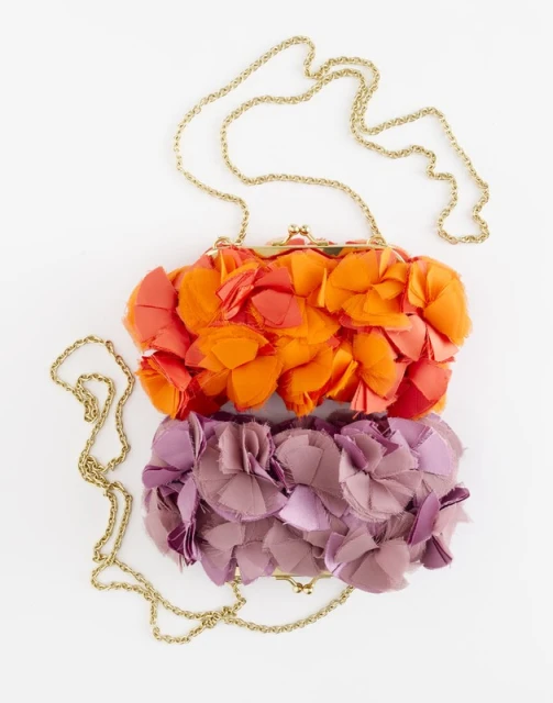 Two flower-embellished clutches with gold chain straps are stacked on a white surface, showcasing orange and purple floral designs.
