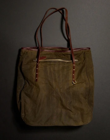 Olive green tote bag with brown leather straps on a dark grey background, showcasing fashion accessory and design.
