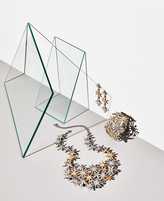 A striking jewelry still life: star-shaped earrings, necklace, and ring beautifully arranged near geometric glass forms.