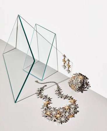 Sparkling star-motif jewellery necklace earrings and bracelet arranged with glass triangle props on white
