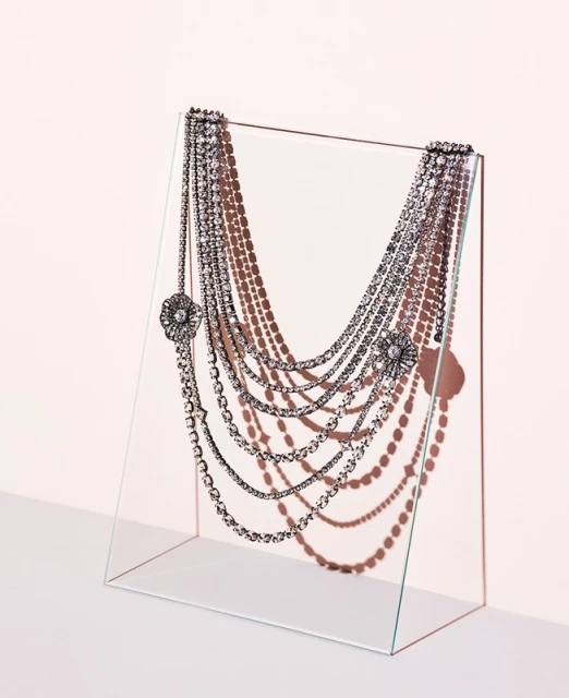 Elegant multi-strand beaded necklace draped over a clear acrylic display stand against a soft pink background, showcasing fashion jewelry.